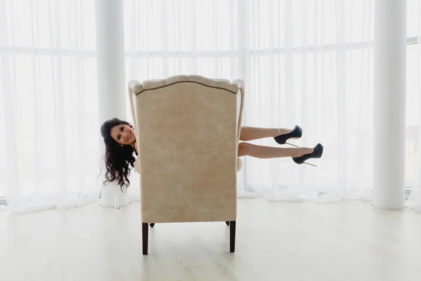Schlanke Brünette auf einem weißen Sessel liegend — Stockfoto