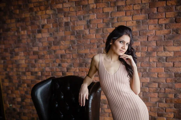 Tall slender brunette next to a armchair — Stock Image Tall slender brunette next to a armchair Stock Picture