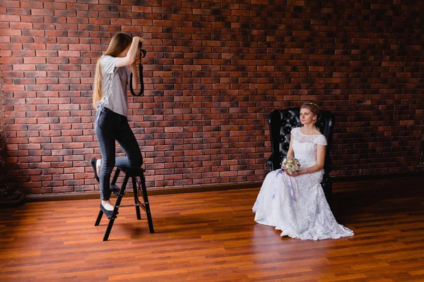 Photographe prenant des photos de la mariée en studio sur un grand fauteuil en cuir — Photo