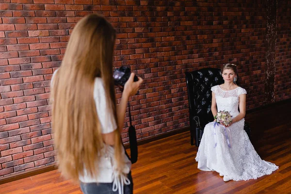 Fotografer mengambil gambar pengantin wanita di studio di atas kursi kulit besar — Stok Foto