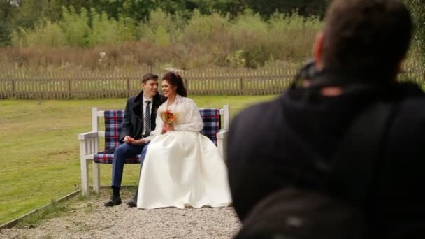 Novomanželé pózuje fotografovi na lavičce — Stock video