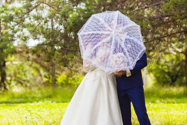 Schönes Brautpaar mit dem weißen Regenschirm — Stockfoto