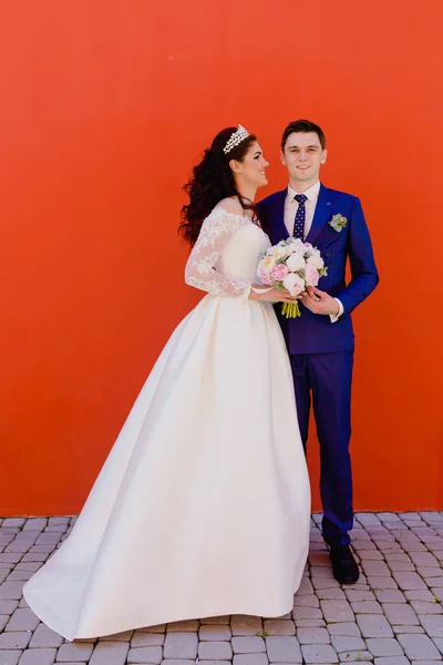 Casal bonito recém-casados perto da parede vermelha — Fotografia de Stock
