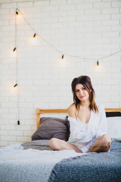 Junge schlanke Brünette sitzt auf einem großen Bett — Stockfoto