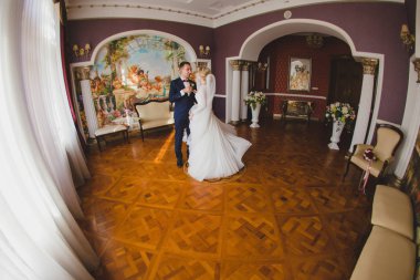 Damat ve gelini büyük salonda parke zeminde dans ediyorlar.