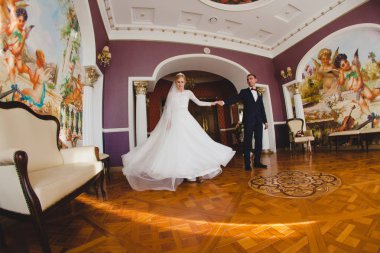 Damat ve gelini büyük salonda parke zeminde dans ediyorlar.