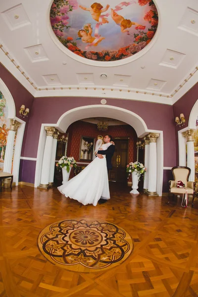 Noivo e sua noiva dançando no chão de parquet no salão grande — Fotografia de Stock