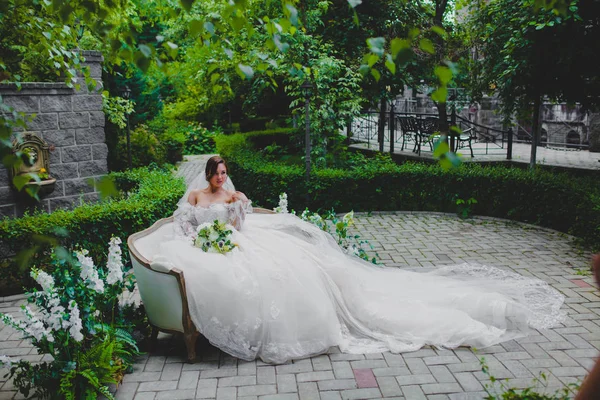Jeune belle mariée en robe de luxe avec un long train assis sur un canapé — Photo