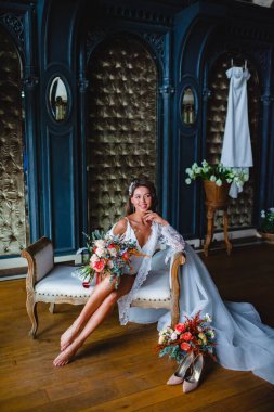 Çekici genç gelin kanepenin üzerinde harika bir gelin buketi ile poz veriyor.