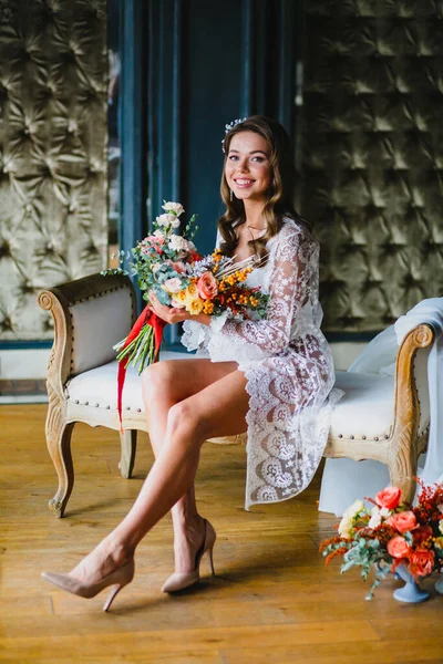 Verführerische junge Braut posiert mit hinreißendem Brautstrauß auf einem Sofa — Stockfoto