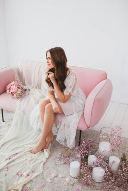 Beyaz gecelikli genç gelin stüdyodaki gül kanepesinde poz veriyor.