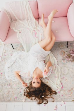 Güzel çıplak bacaklı genç gelin büyük beyaz stüdyoda yerde poz veriyor.