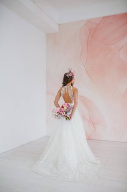 Beyaz elbiseli, başında çiçek çelengi olan genç gelin stüdyoda poz veriyor.