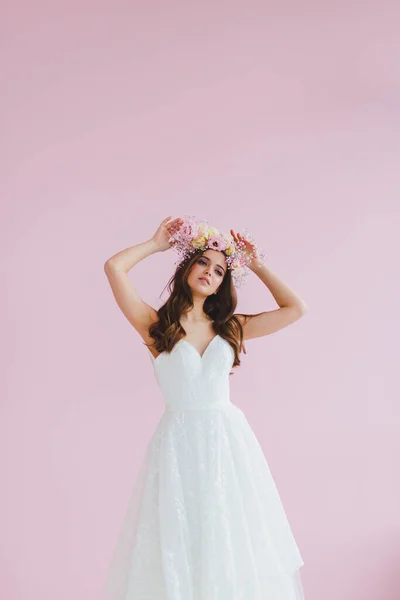 Giovane sposa in abito bianco con corona di fiori sulla testa in posa in studio Fotografia Stock