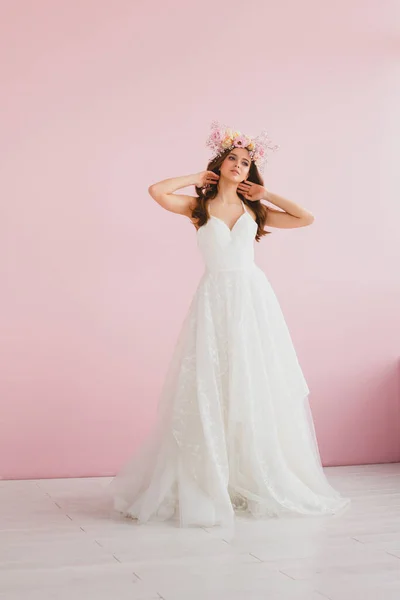 Giovane sposa in abito bianco con corona di fiori sulla testa in posa in studio Fotografia Stock