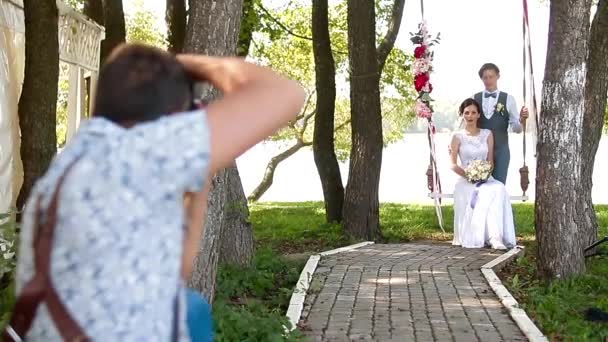 Wedding photographer taking pictures couple of newlyweds on a rope swing — Stock Video
