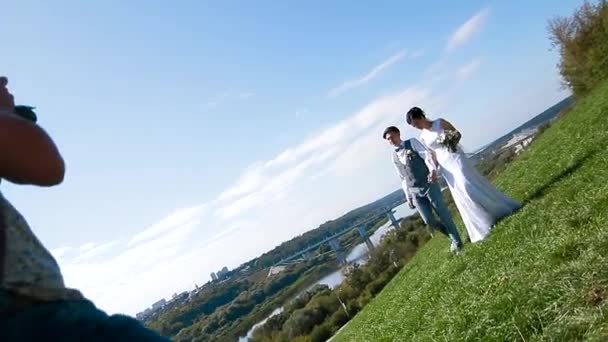 Wedding photographer taking pictures of the bride and groom on a hillside — Stock Video