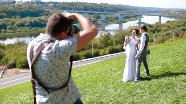 Wedding photographer taking pictures of the bride and groom on a hillside — 비디오