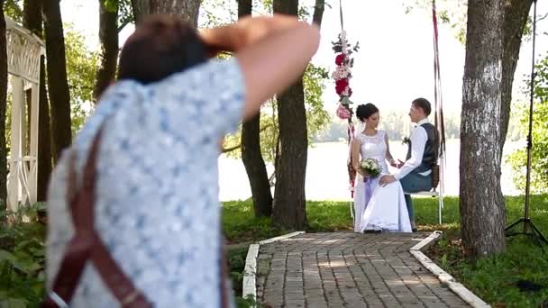Свадебный фотограф фотографирует парочку молодоженов на качелях — стоковое видео