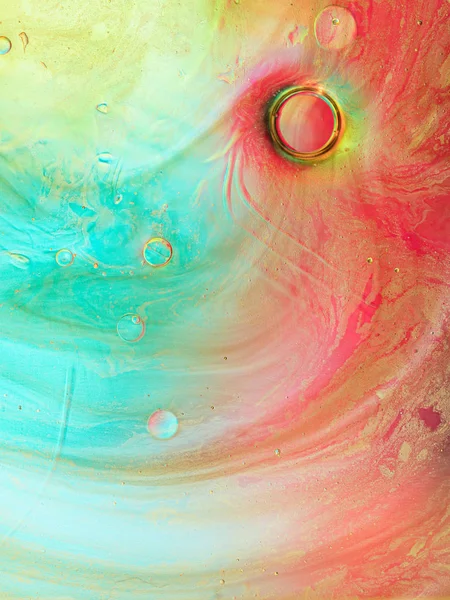 Gold glitter and drops of oil on surface of water. Abstract colorful liquid macro background.