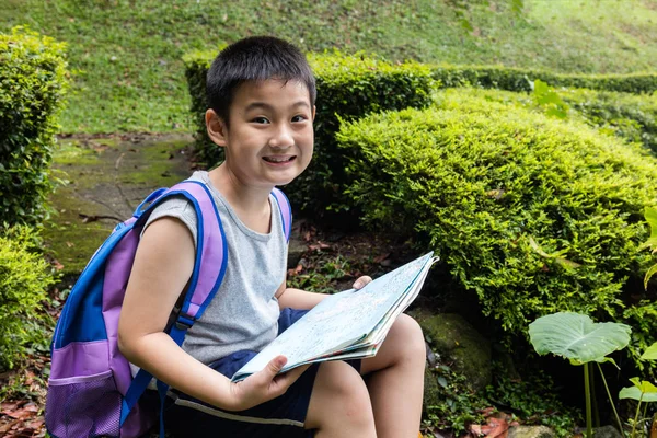 Smiling Asian Chinese boy holding map sitting in the forest