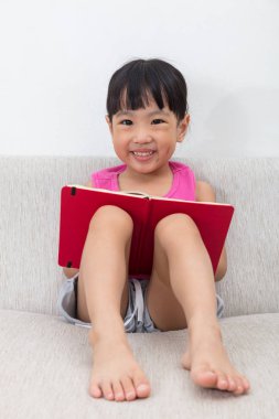 Mutlu Asyalı Çinli küçük kız kitap ile kanepede oturan