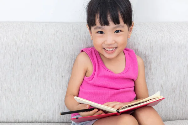 Ευτυχισμένος Ασίας κινεζική μικρό κορίτσι που κάθεται στο καναπέ γραφής βιβλίο — Φωτογραφία Αρχείου