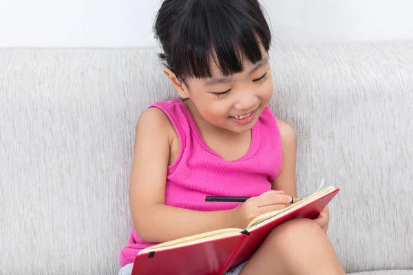 Glücklich asiatische chinesische kleine Mädchen sitzen auf Sofa Schreiben Buch — Stockfoto