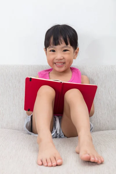 Glücklich asiatische chinesische kleines Mädchen sitzt auf Sofa mit Buch — Stockfoto