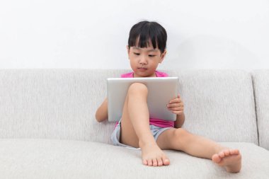 Asyalı Çinli küçük kız tablet ile kanepede oturan