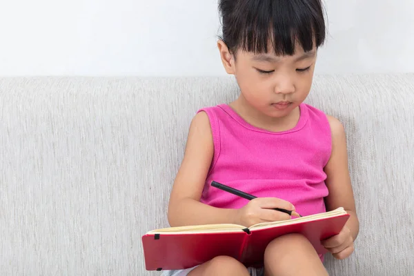 Ασίας κινεζική μικρό κορίτσι που κάθεται στο καναπέ γραφής βιβλίο — Φωτογραφία Αρχείου