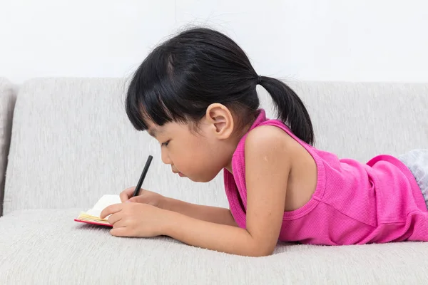Ασιατική Κινέζικη κοριτσάκι τοποθέτηση στο καναπέ γραφής βιβλίο — Φωτογραφία Αρχείου