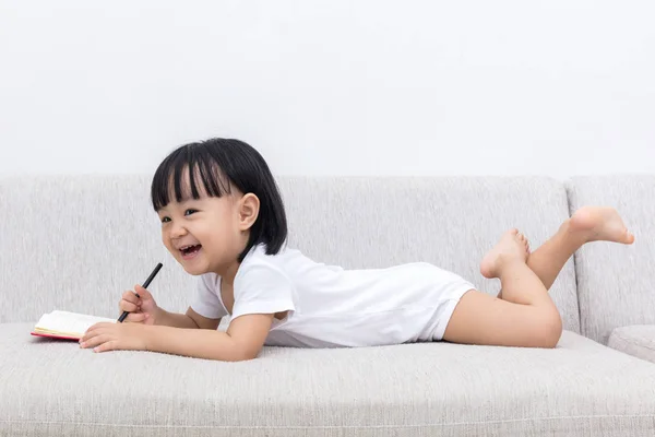 Glad asiatiska kinesiska liten flicka handpåläggning soffa skriva bok — Stockfoto