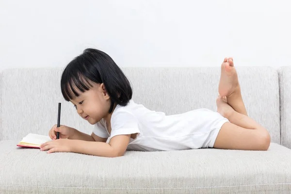 Ασιατική Κινέζικη κοριτσάκι τοποθέτηση στο καναπέ γραφής βιβλίο — Φωτογραφία Αρχείου