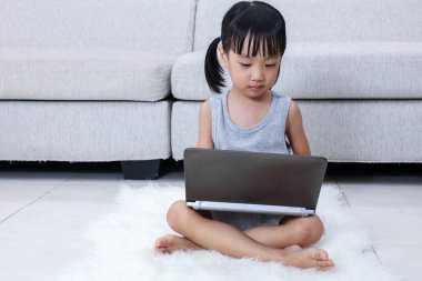 Asyalı Çinli küçük kız yere dizüstü bilgisayar kullanarak
