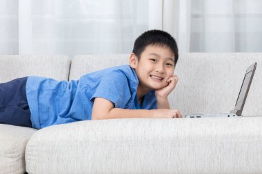 Mutlu Asyalı Çinli küçük çocuk kanepede dizüstü bilgisayar kullanarak