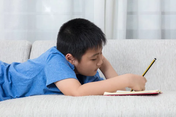 Annoiato asiatico cinese bambino scrittura libro su il divano — Foto Stock