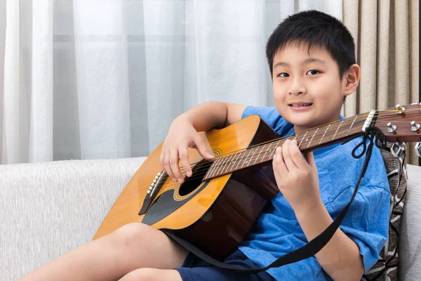 Ευτυχισμένος Ασίας κινεζική μικρό αγόρι που παίζει κιθάρα στον καναπέ — Φωτογραφία Αρχείου