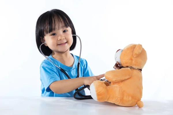 Счастливая азиатская китайская девочка-доктор осмотрит плюшевого мишку — стоковое фото