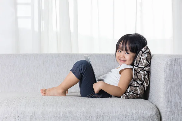 Felice asiatica bambina cinese sdraiata sul divano con tablet — Foto Stock