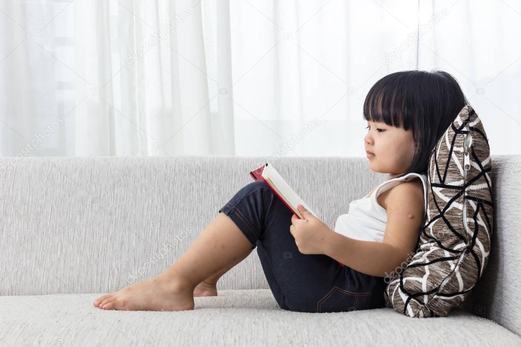 Asian Chinese little girl reading book on the sofa