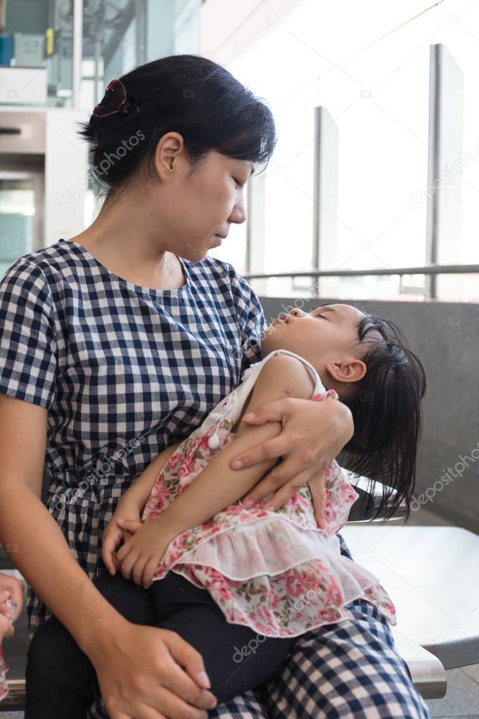 Asian Chinese mother carrying sleeping daughter inside a MRT sta