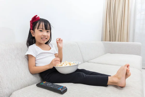 Felice asiatico cinese bambina mangiare popcorn sul divano — Foto Stock
