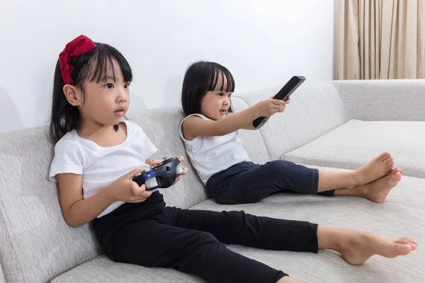 Asian Chinese little sisters playing TV games on the sofa