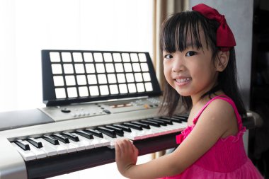 Happy Asian Chinese little girl playing electric piano keyboard  clipart