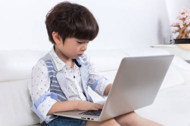 Dizüstü bilgisayar ile kanepede oturan Asya Çin küçük çocuk