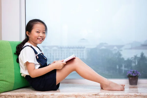 Asiatico cinese bambina lettura libro sul davanzale della finestra — Foto Stock