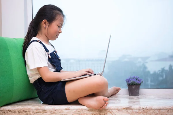 Asiatisch chinesisch klein mädchen using laptop auf die fensterbank — Stockfoto