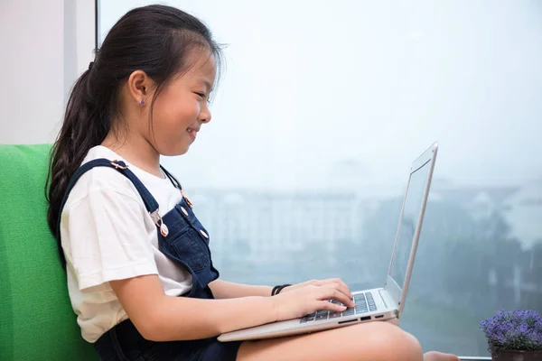 Asiatisch chinesisch klein mädchen using laptop auf die fensterbank — Stockfoto