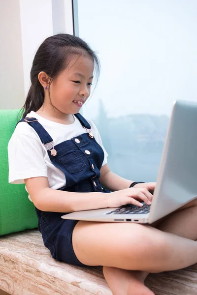 Asiatisch chinesisch klein mädchen using laptop auf die fensterbank — Stockfoto